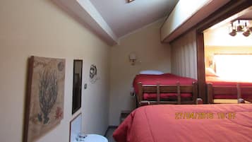 Una habitación pequeña y acogedora con tragaluz, una cama con manta roja, una mesita de noche y un espejo fijado a la pared.
