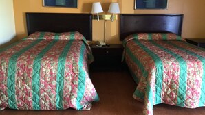 Habitación de hotel con dos camas, cada una con una colcha estampada con motivos florales, una mesita de noche entre ellas y dos lámparas fijadas a la pared.