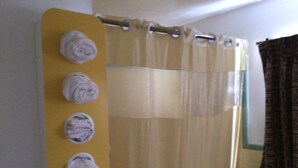 Un baño con un perchero amarillo que sostiene cuatro toallas, una cortina de ducha y una cortina marrón.