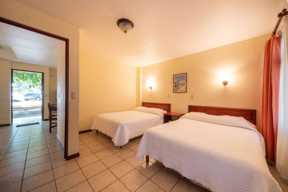 A hotel room with two beds, a door leading to a balcony, and a small table.