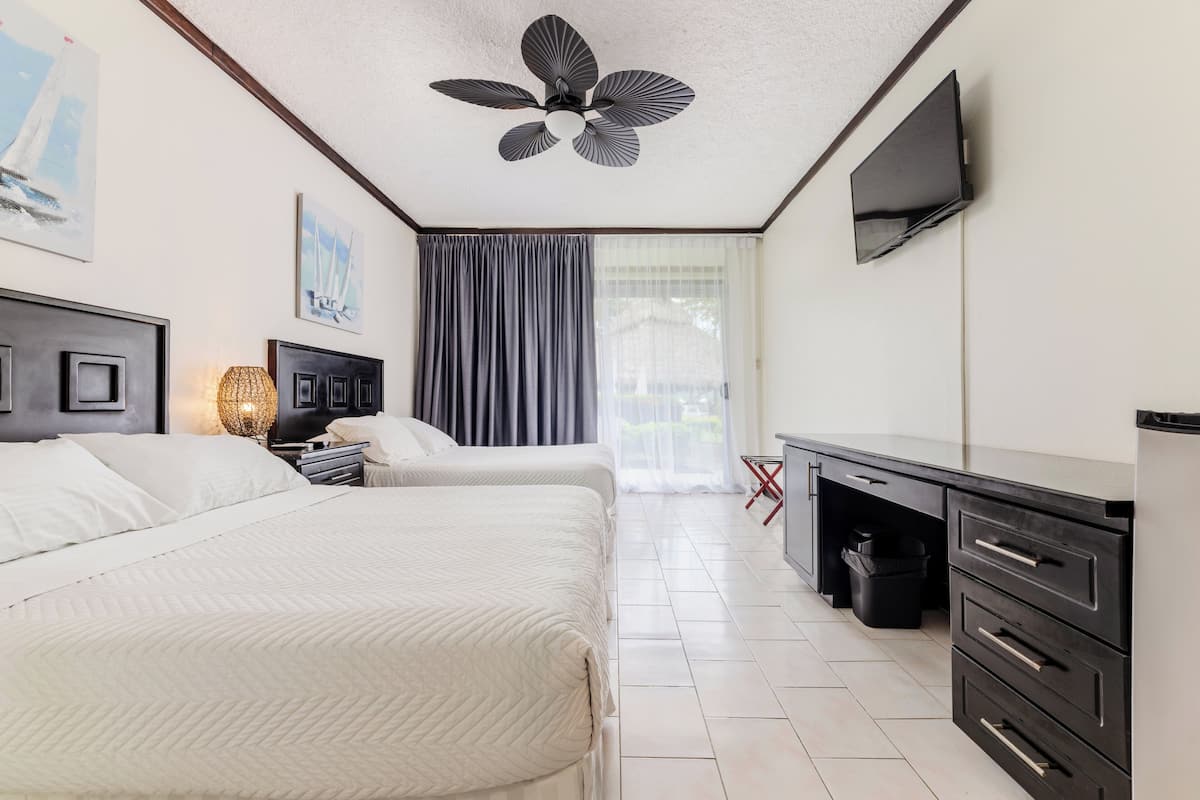 A hotel room with two beds, a ceiling fan, a TV, a desk, and a window with curtains.