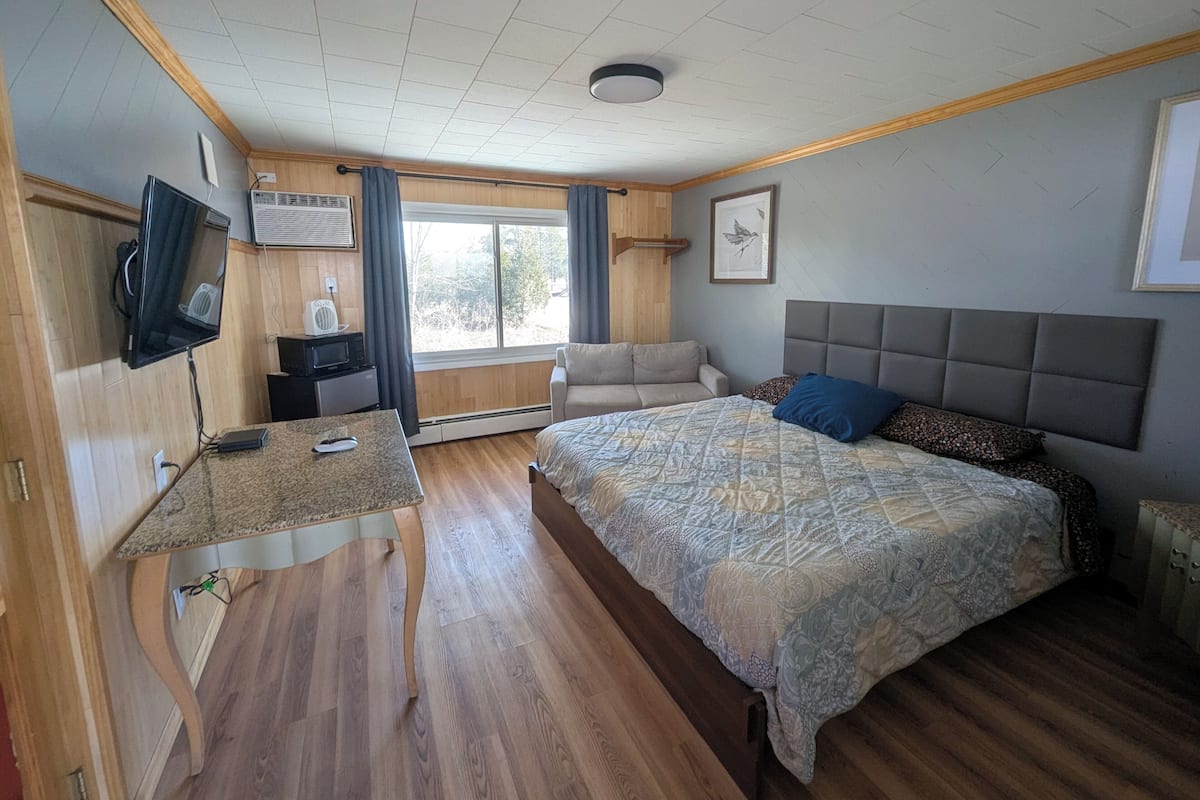 A bedroom with a bed, a desk, a television, and a window.