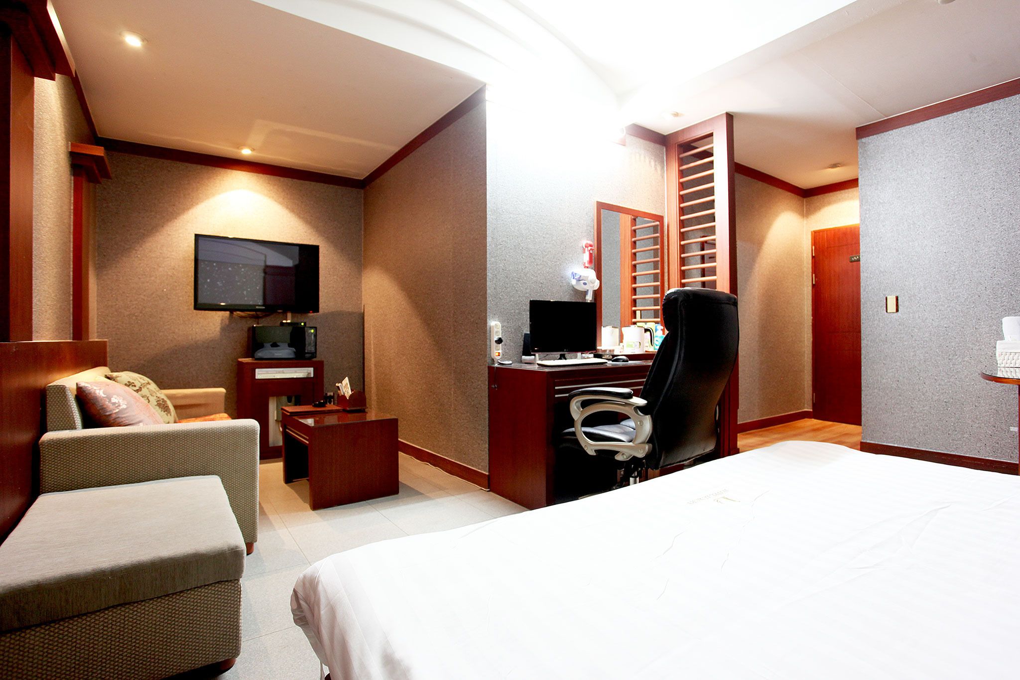 A hotel room with a bed, a desk with a computer, a chair, a TV, and a small table.