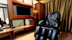 A massage chair in a room with a TV, wooden cabinet, and a vase with flowers.