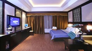 A hotel room with a bed, a desk with a computer, a television, and a large window with curtains.