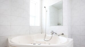 A white bathtub with a handheld showerhead, a mirror above it, and white tiled walls.