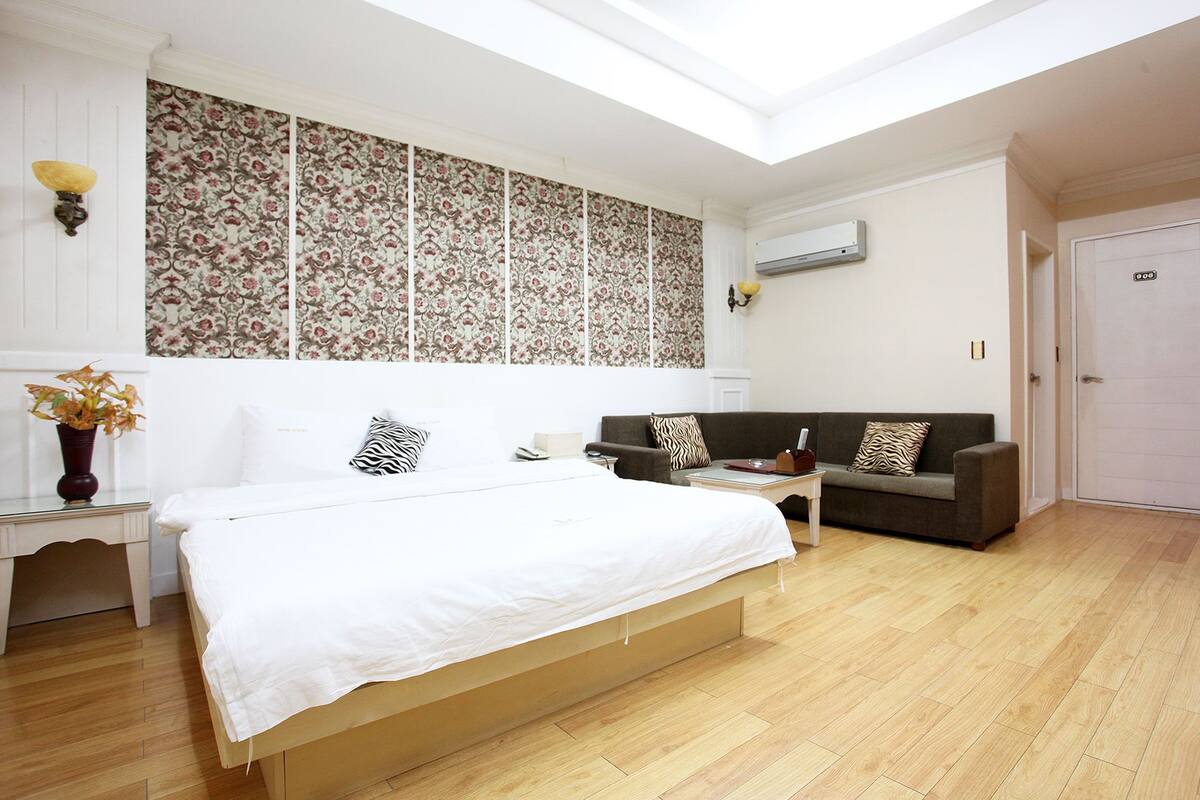 Un dormitorio con una cama grande, un sofá, una mesita y un panel decorativo en la pared.