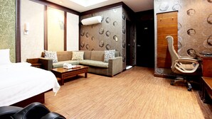 A hotel room with a bed, a sofa, a coffee table, and a desk with a chair.