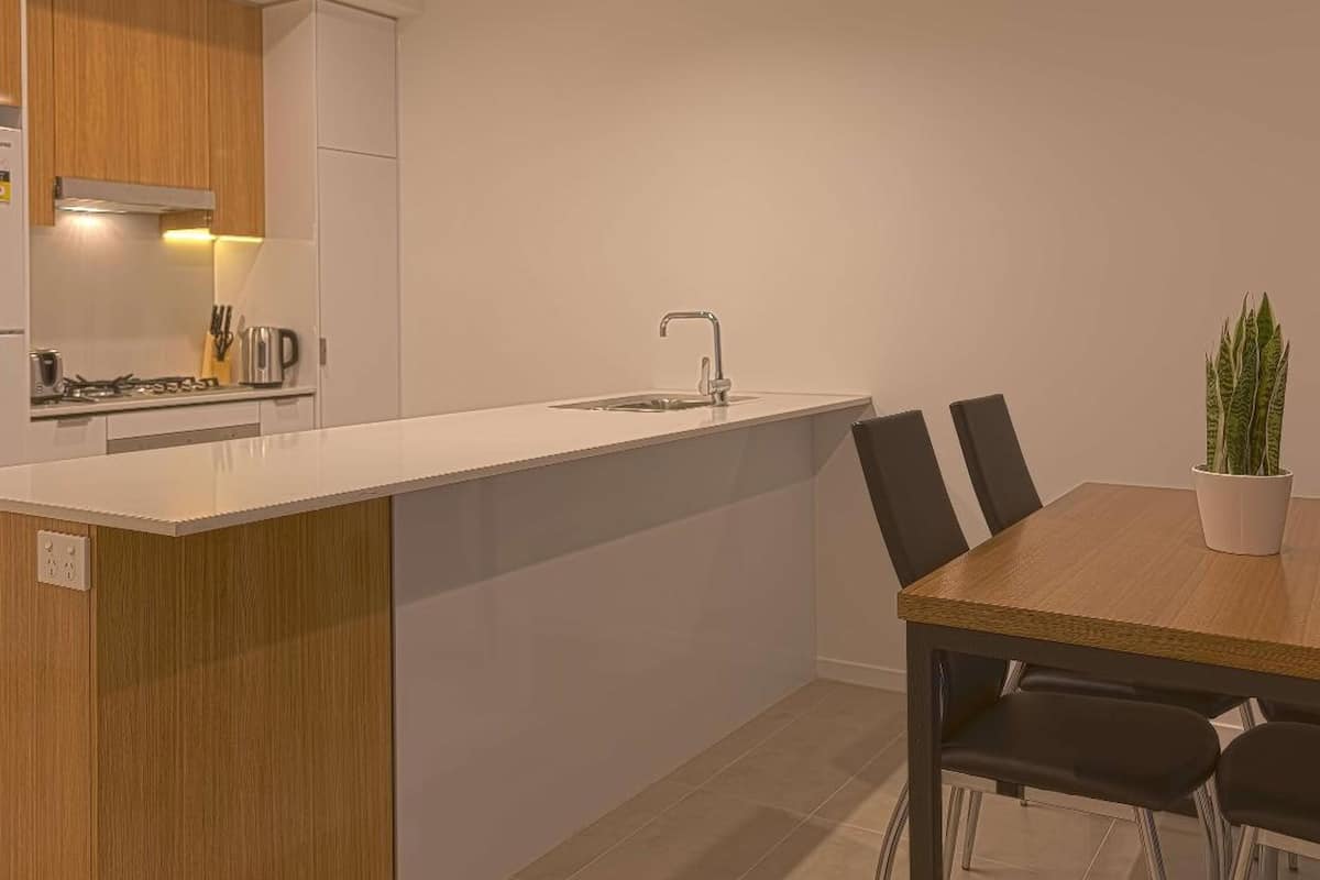 A compact kitchen with a white countertop, a sink, and a stove. There is a dining table with chairs and a potted plant.