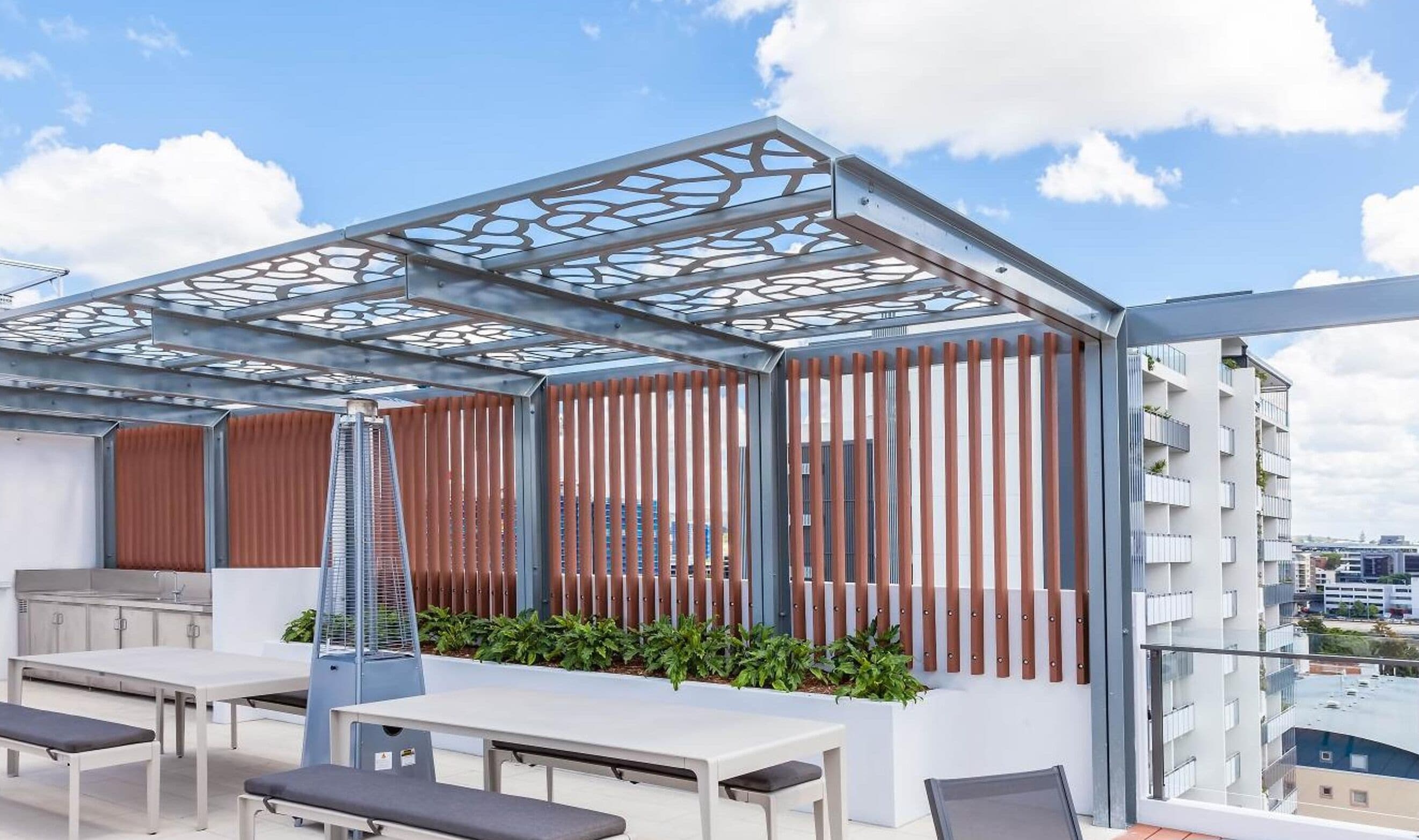 Een terras buiten met een modern ontwerp, met een metalen pergola, houten lamellen en een zithoek met tafels en banken.