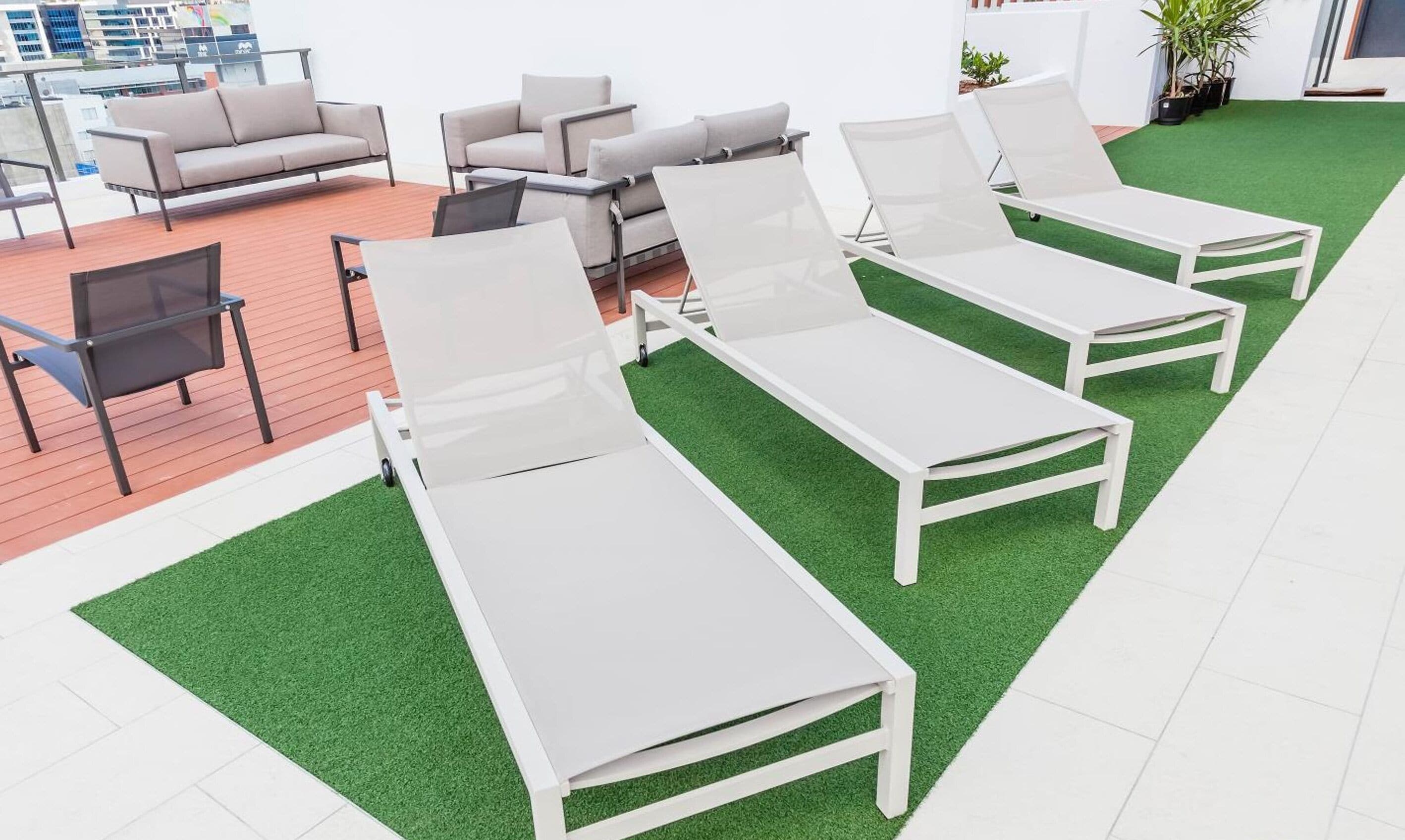 Een moderne buitenlounge met witte loungestoelen en een bank, voorzien van kunstgras en uitzicht op de stad.