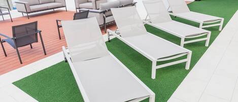 Een moderne buitenlounge met witte loungestoelen en een bank, voorzien van kunstgras en uitzicht op de stad.