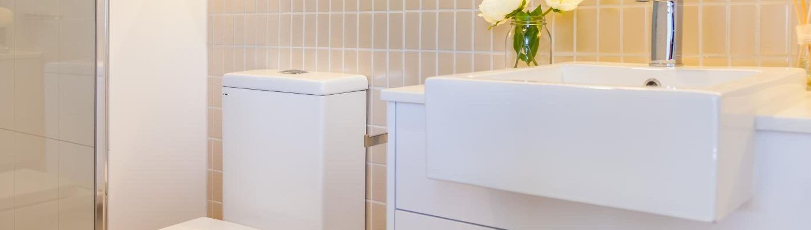 Un baño con inodoro, lavamanos y un florero con flores.