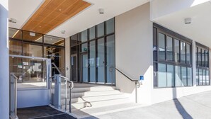 Una entrada de edificio moderna con puertas de cristal, techo de madera y una escalera que conduce al piso superior.