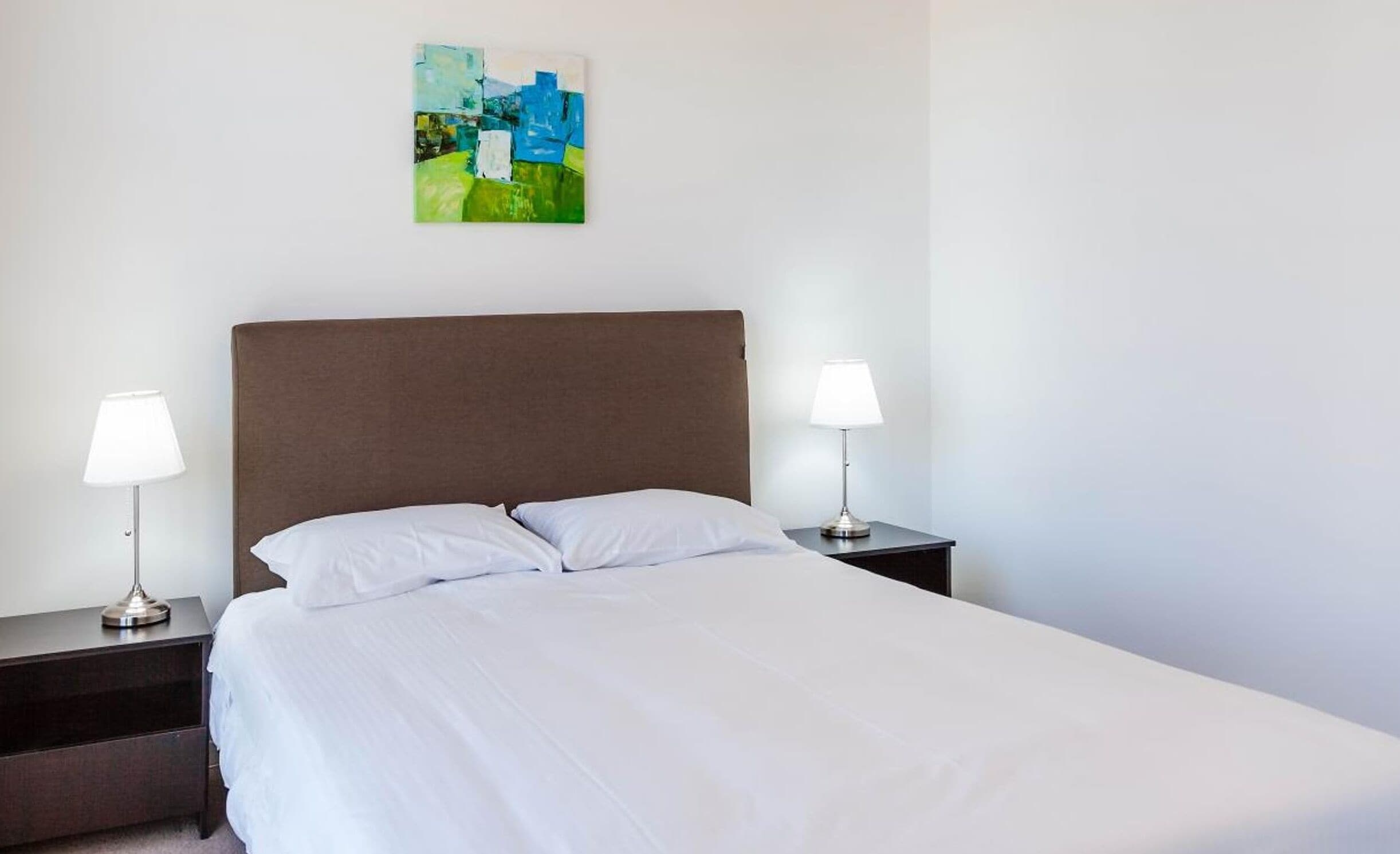 A hotel room with a large bed, two bedside tables with lamps, and a painting on the wall.