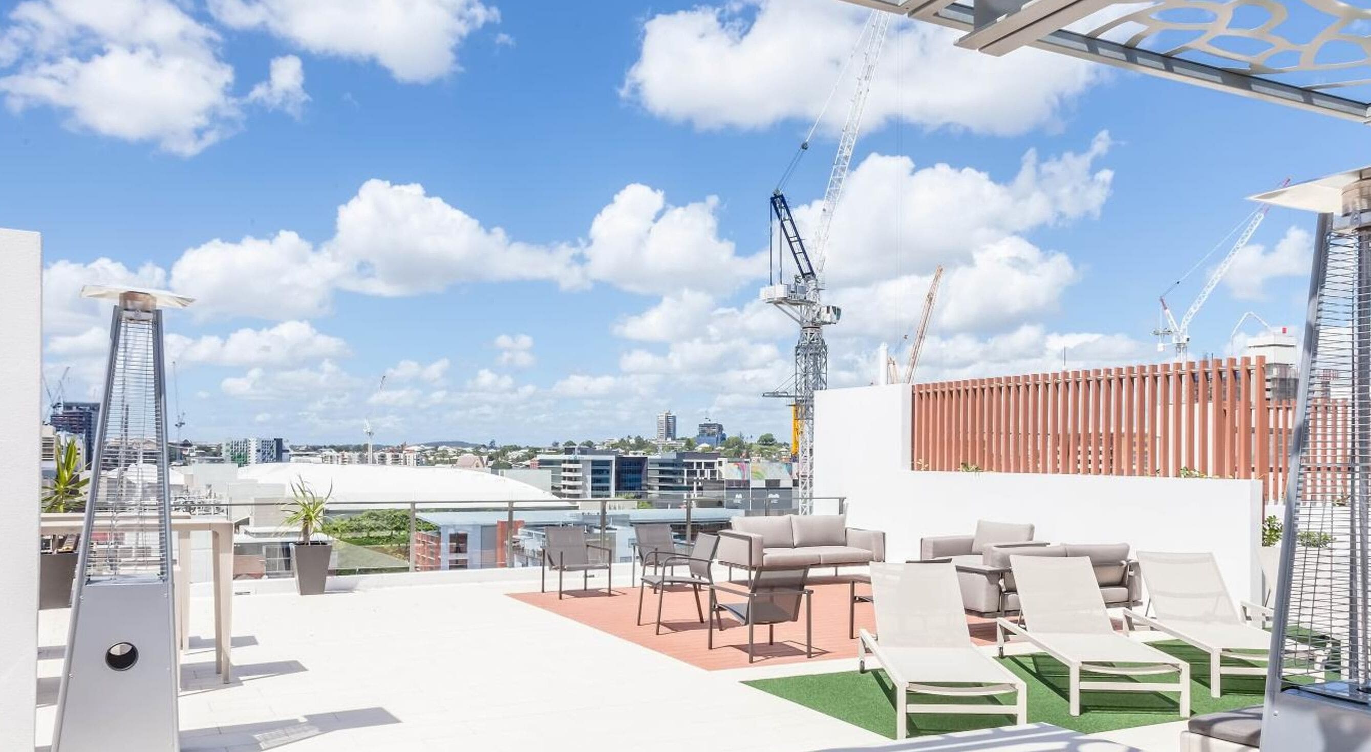 A rooftop terrace with outdoor seating, a view of the cityscape, and a crane in the background.