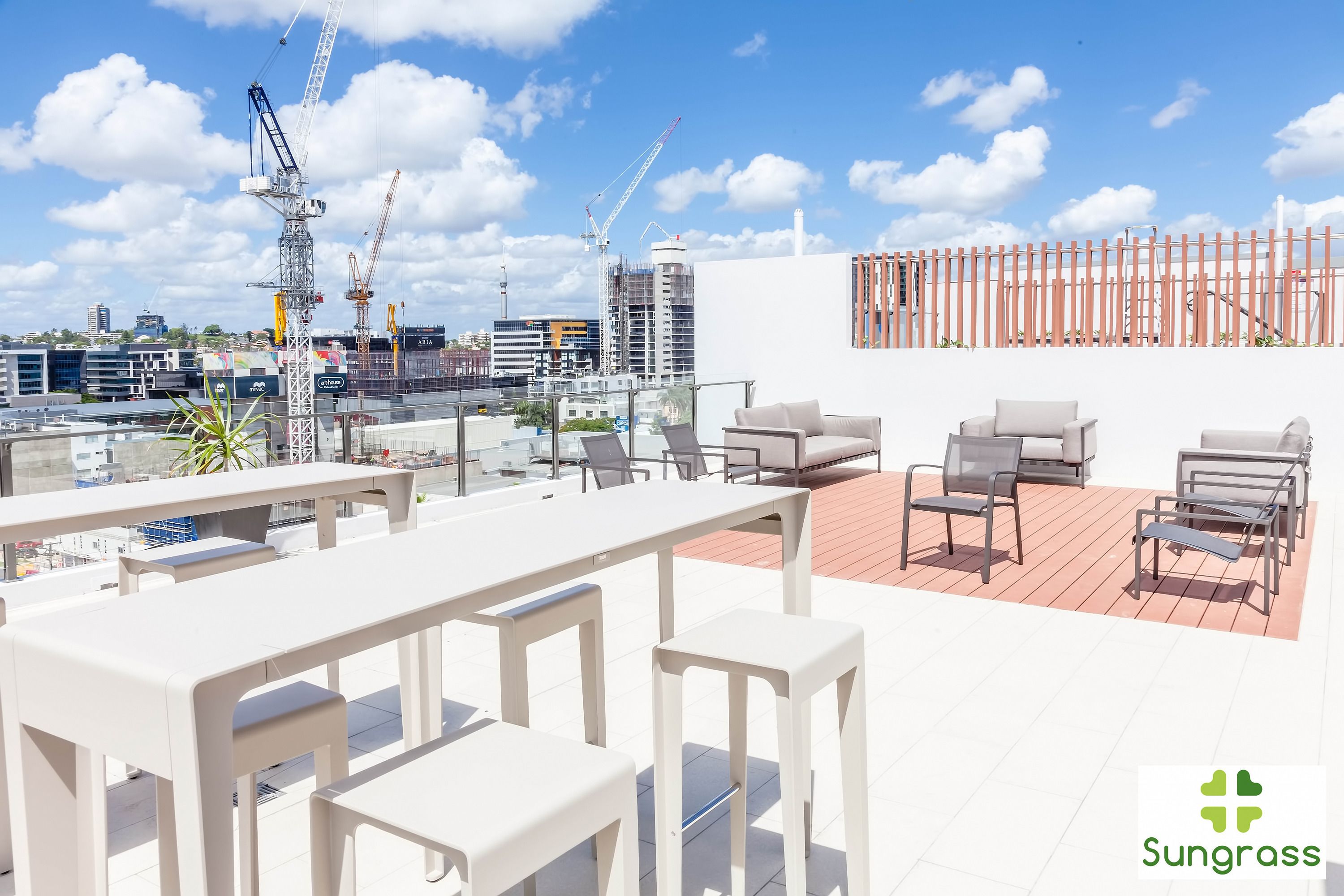 Terraço no telhado com mobiliário branco, vista do horizonte da cidade e guindastes ao fundo.