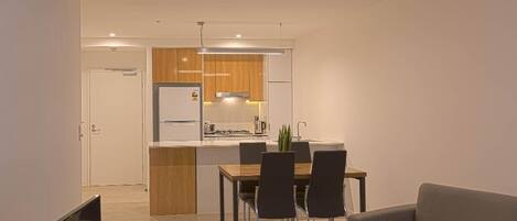A modern kitchen with a dining area, a ceiling fan, and a grey sofa with a vase of red flowers.