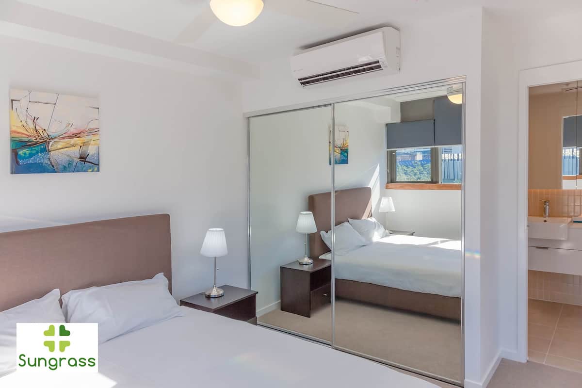 A hotel room with a bed, bedside tables, a mirror, and artwork on the wall.