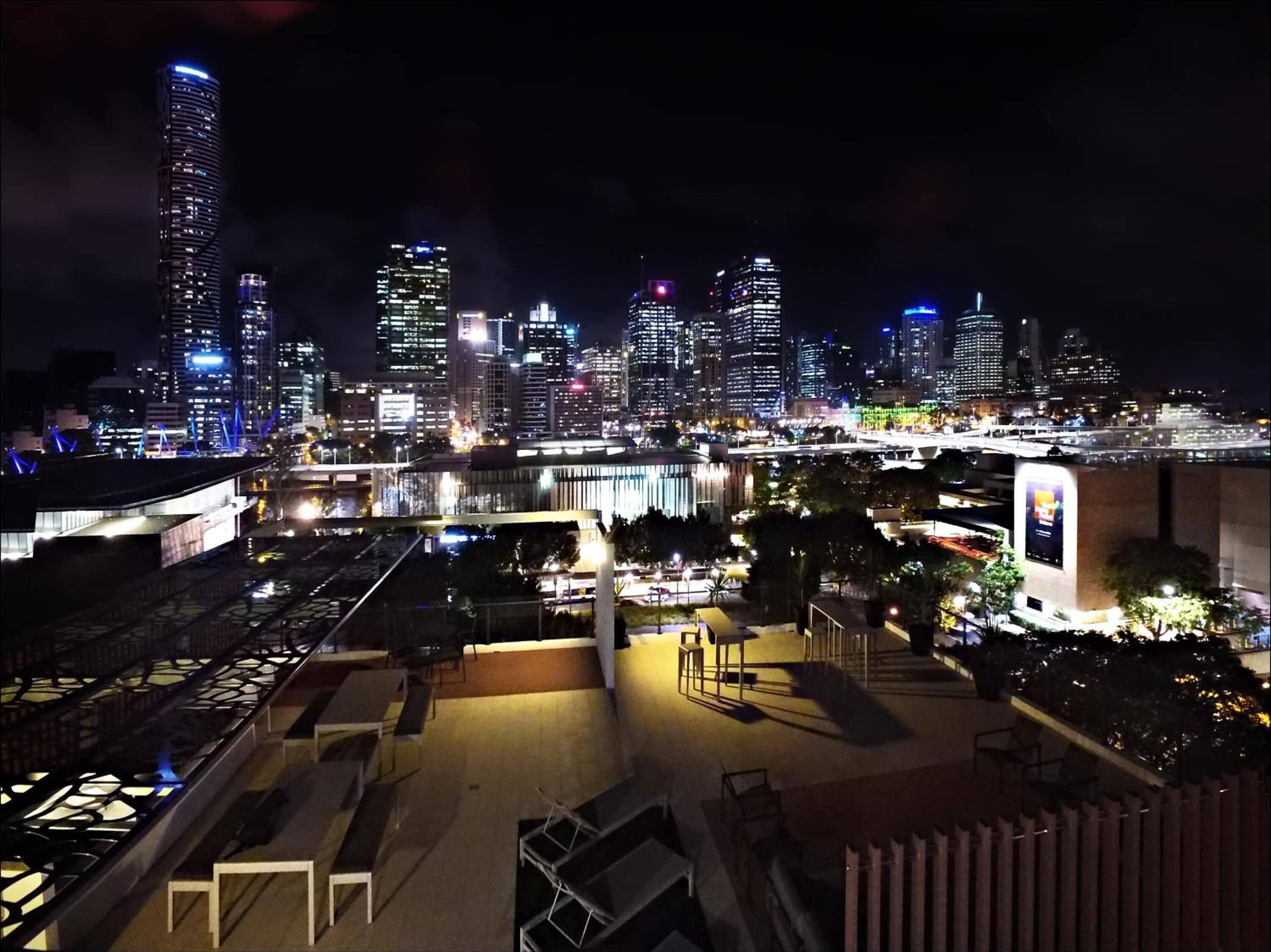 A nighttime cityscape with illuminated skyscrapers and a bridge.