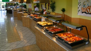 Un espace buffet comprenant plusieurs stands de nourriture, un chef cuisinier et un comptoir avec une caisse enregistreuse.