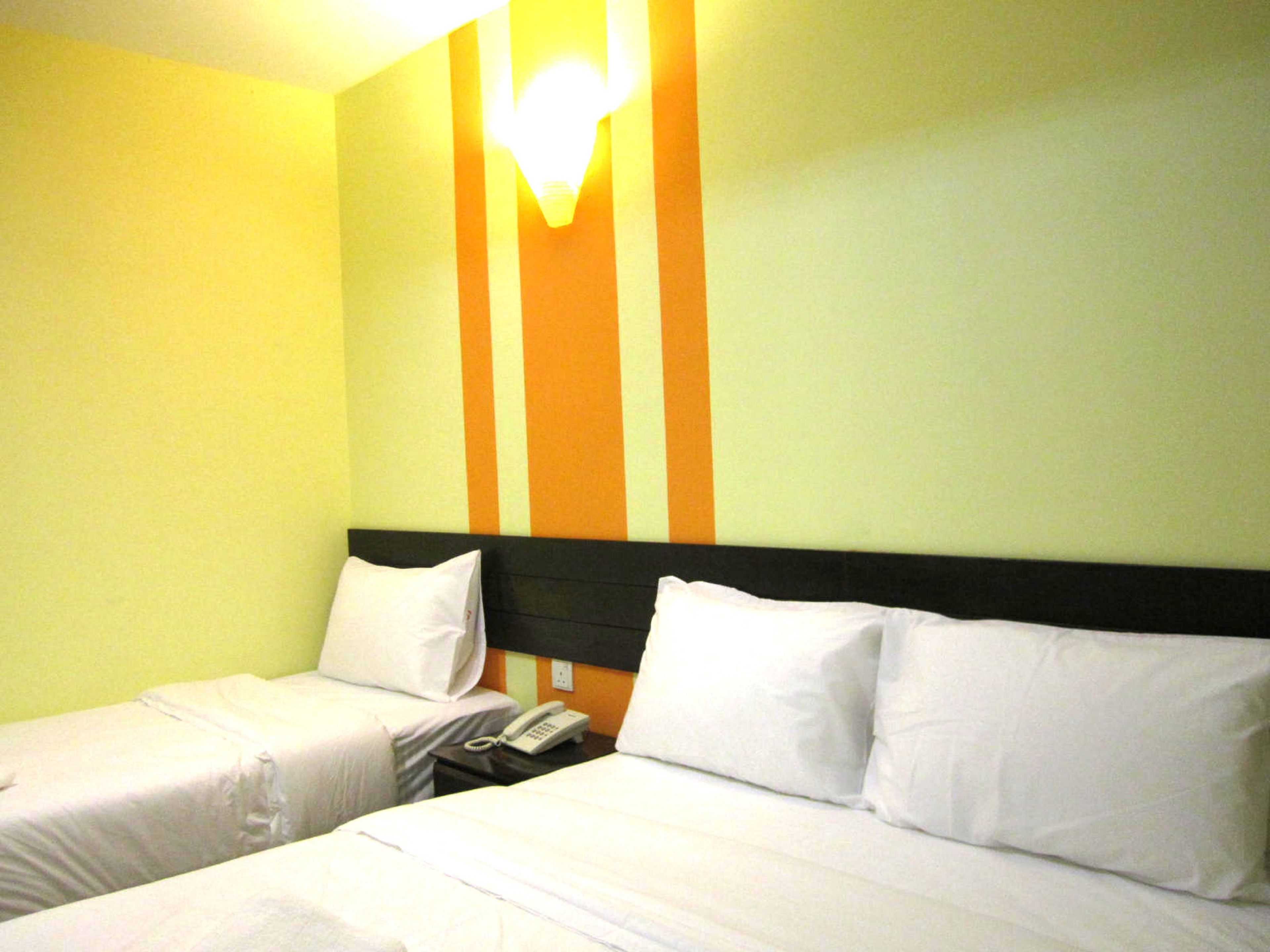 Ein Hotelzimmer mit zwei Betten, jeweils mit weißer Bettwäsche und Kissen. Auf dem Nachttisch zwischen den Betten steht ein Telefon. Die Wände sind hellgrün gestrichen mit einem orangefarbenen Streifenmuster.