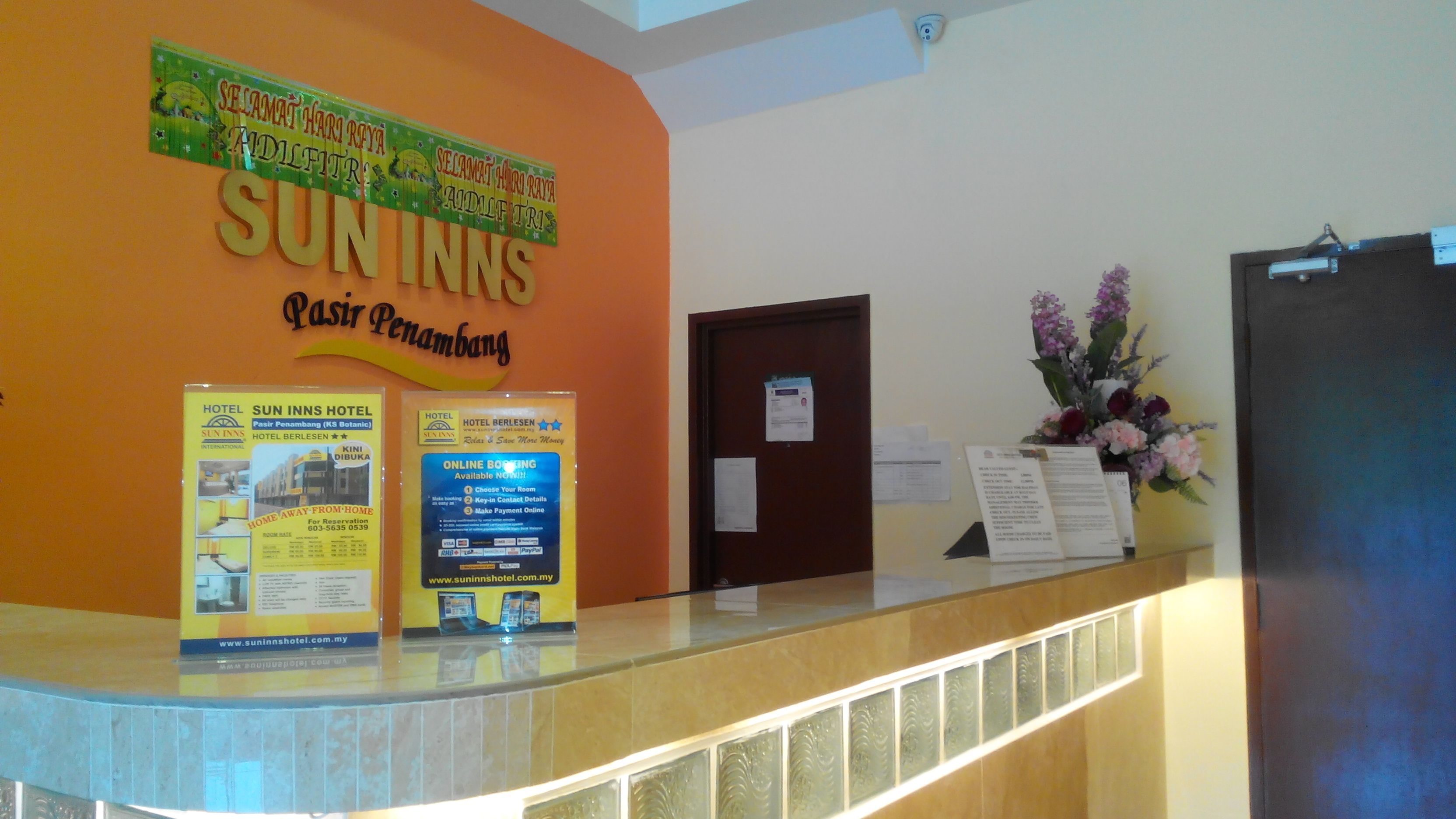A reception desk with a sign for Sun Inn Pasir Penambang, featuring a reception area, a door, and a floral arrangement.