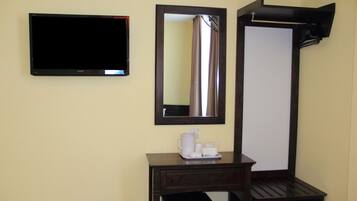 A hotel room with a flat-screen TV, a large mirror, a small desk with a coffee maker, and a trash bin.