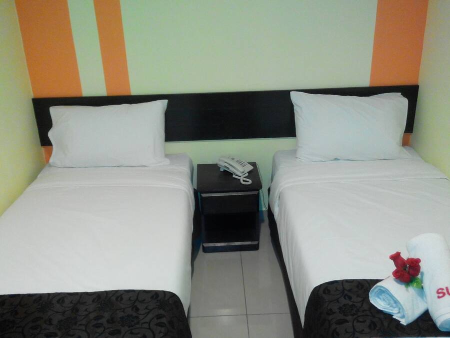 A twin room with two beds, a bedside table with a phone, and a towel with a rose and the word "SUN" on it.