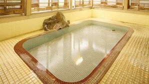 Una amplia piscina interior con suelo de baldosas y paredes de madera, rodeada de ventanas.