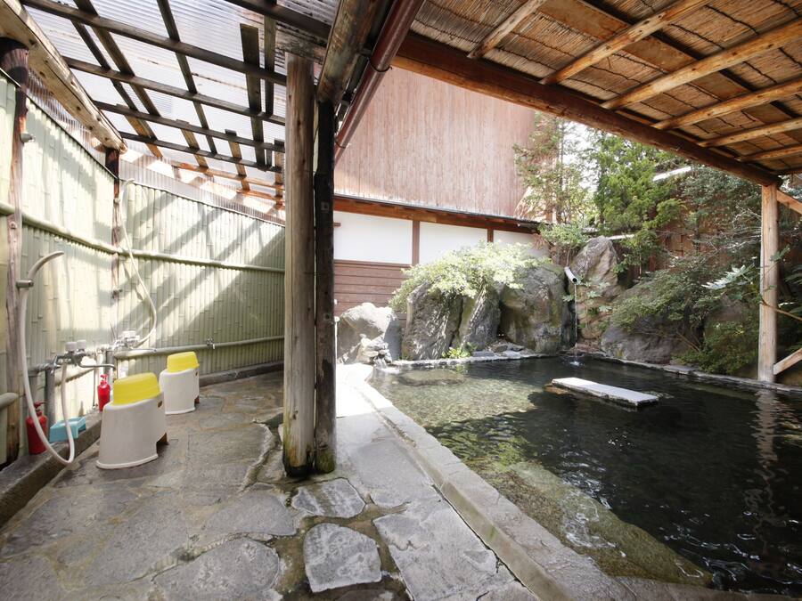 A traditional Japanese onsen with stone flooring, a wooden roof, and a small pond.