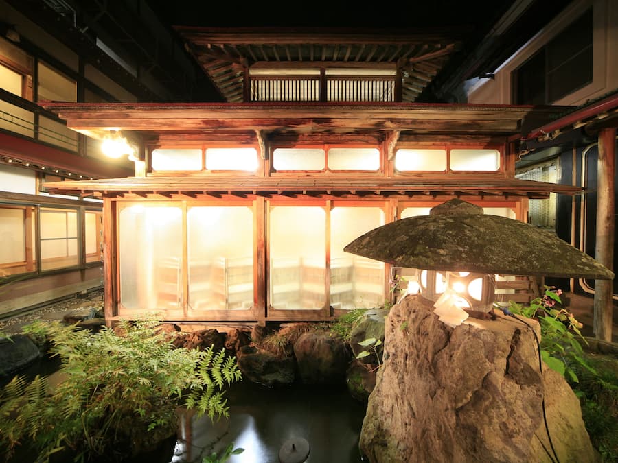 A traditional Japanese building with a wooden structure, a stone lantern, and a water feature with plants.