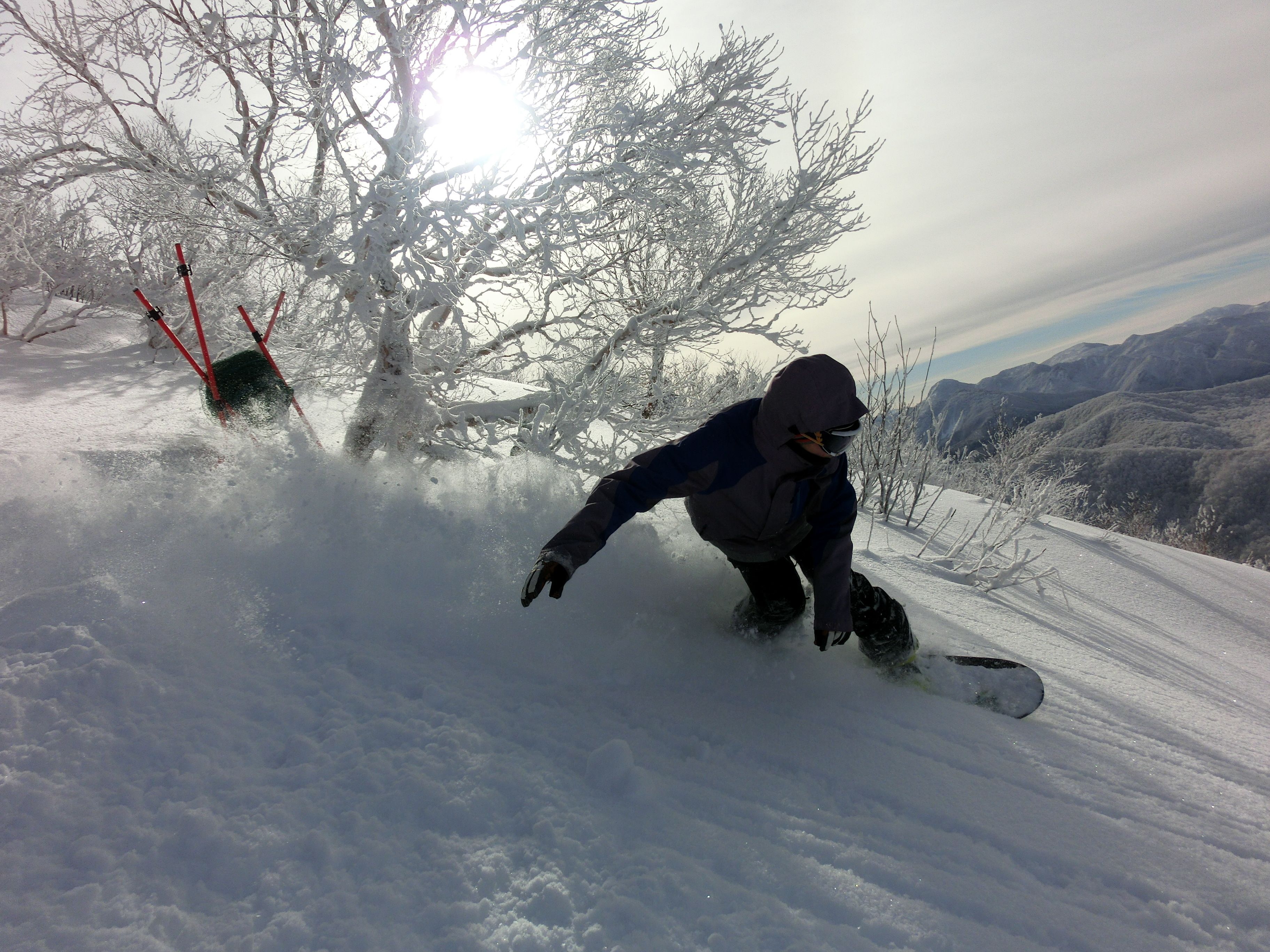 A snowboarder on a snowy slope with a clear sky and mountains in the background.