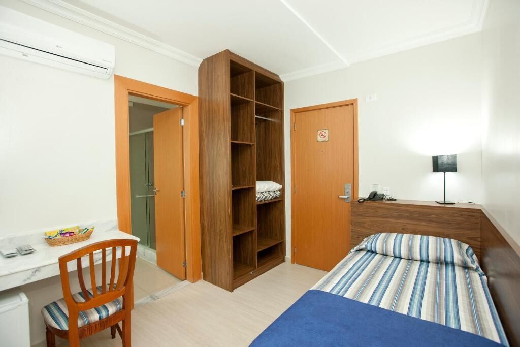 Un dormitorio con una cama, un escritorio con una silla, un armario y una mesita de noche con una lámpara.