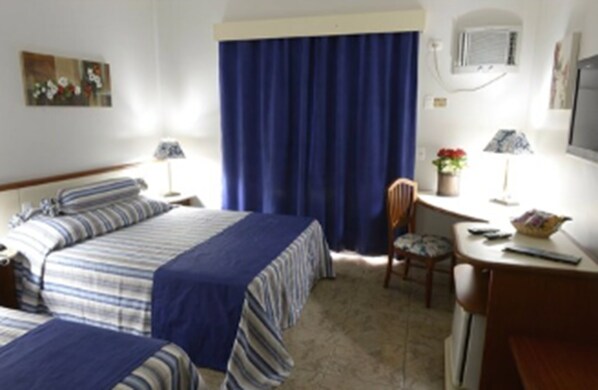 A hotel room with two beds, a desk, a chair, a table, and a window with curtains. - Hotel Colonial Plaza (Itu)