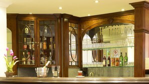Un coin bar avec un lambris en bois, deux tabourets de bar et une vitrine en verre contenant des bouteilles.