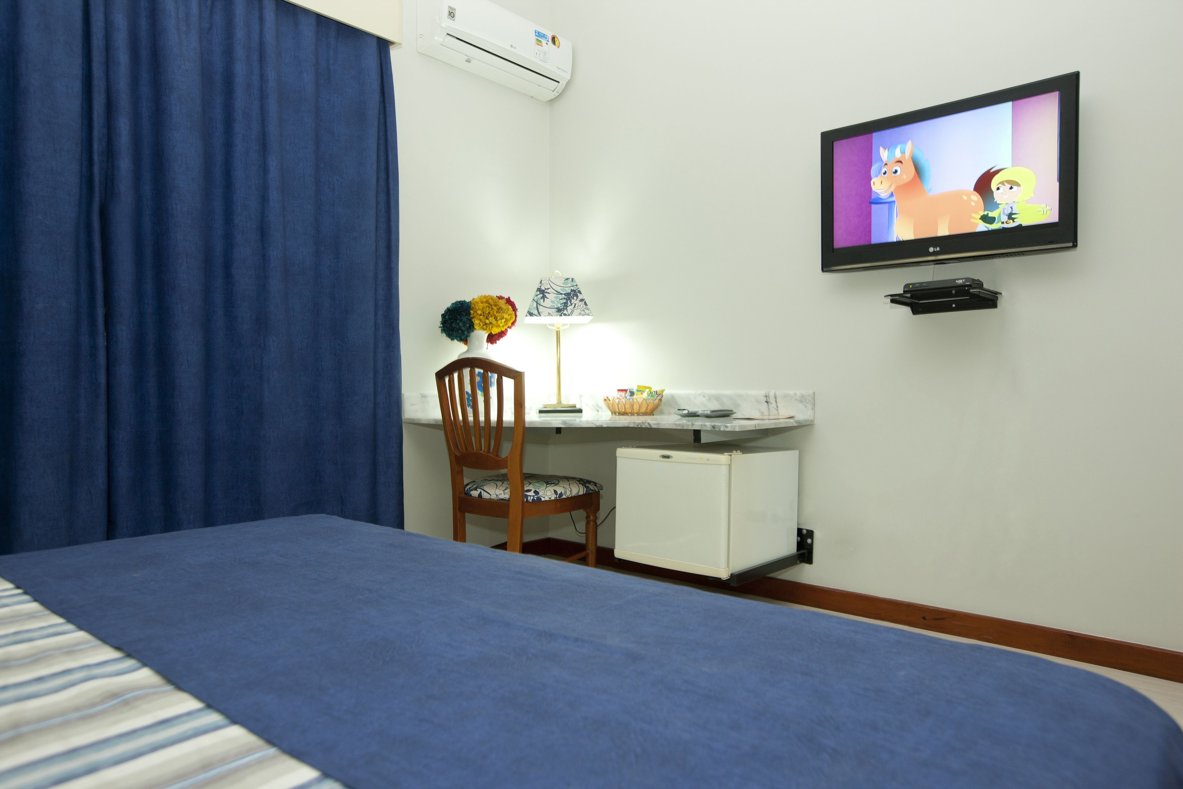 Una habitación de hotel con una cama, un escritorio con lámpara, televisor y un refrigerador pequeño.