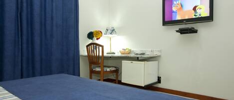 A hotel room with a bed, a desk with a lamp, a television, and a small refrigerator.