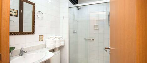 Un baño con lavamanos de mármol, inodoro, cabina de ducha con paredes de vidrio y espejo con marco decorativo.