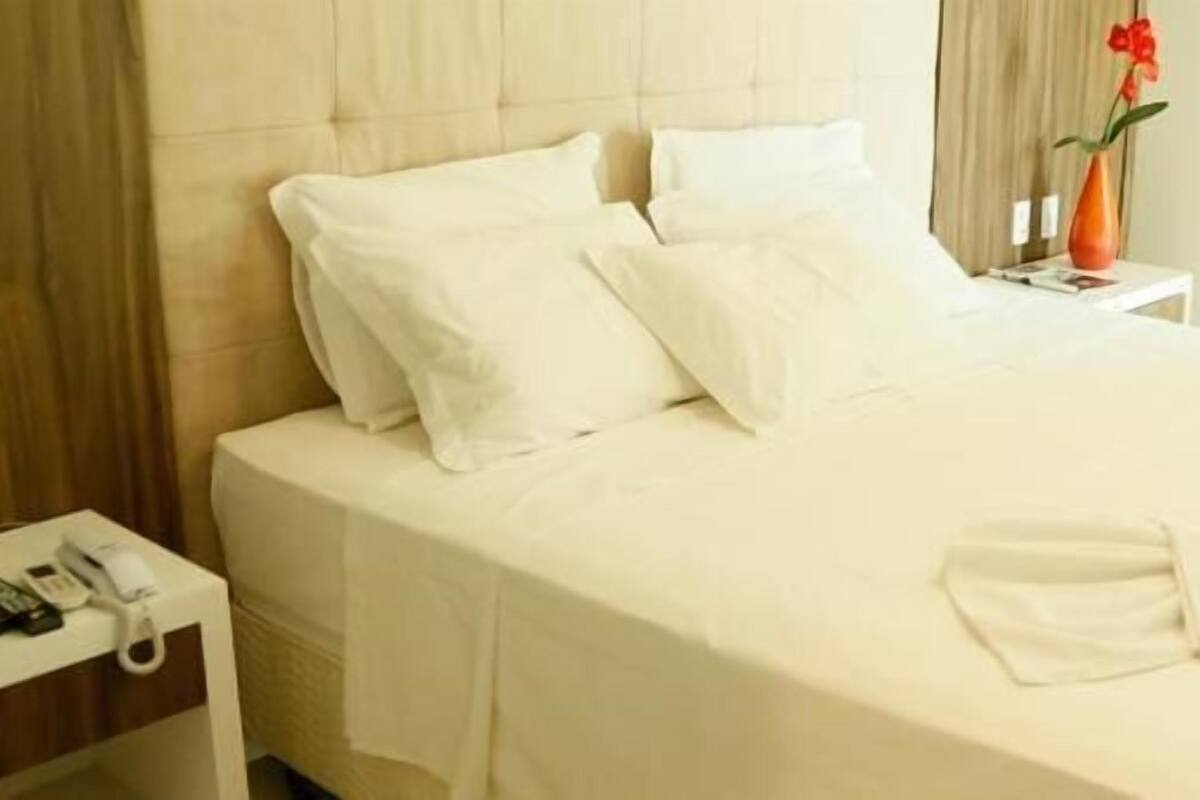 A neatly made bed with white linens, a bedside table with a vase of flowers, and a telephone.