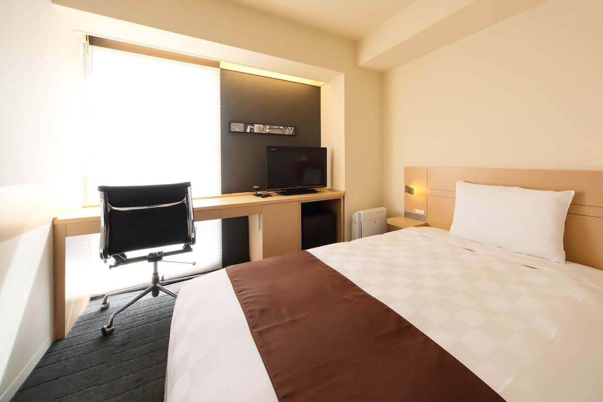 Ein Hotelzimmer mit einem Bett, einem Schreibtisch mit Computer, einem Sessel und einem Fernseher.