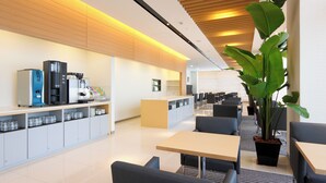 A modern, well-lit cafe with a long counter, seating area, and a large potted plant.