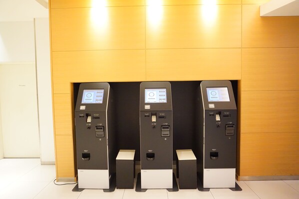 Three self-service kiosks in a modern, well-lit room with a wooden accent wall.