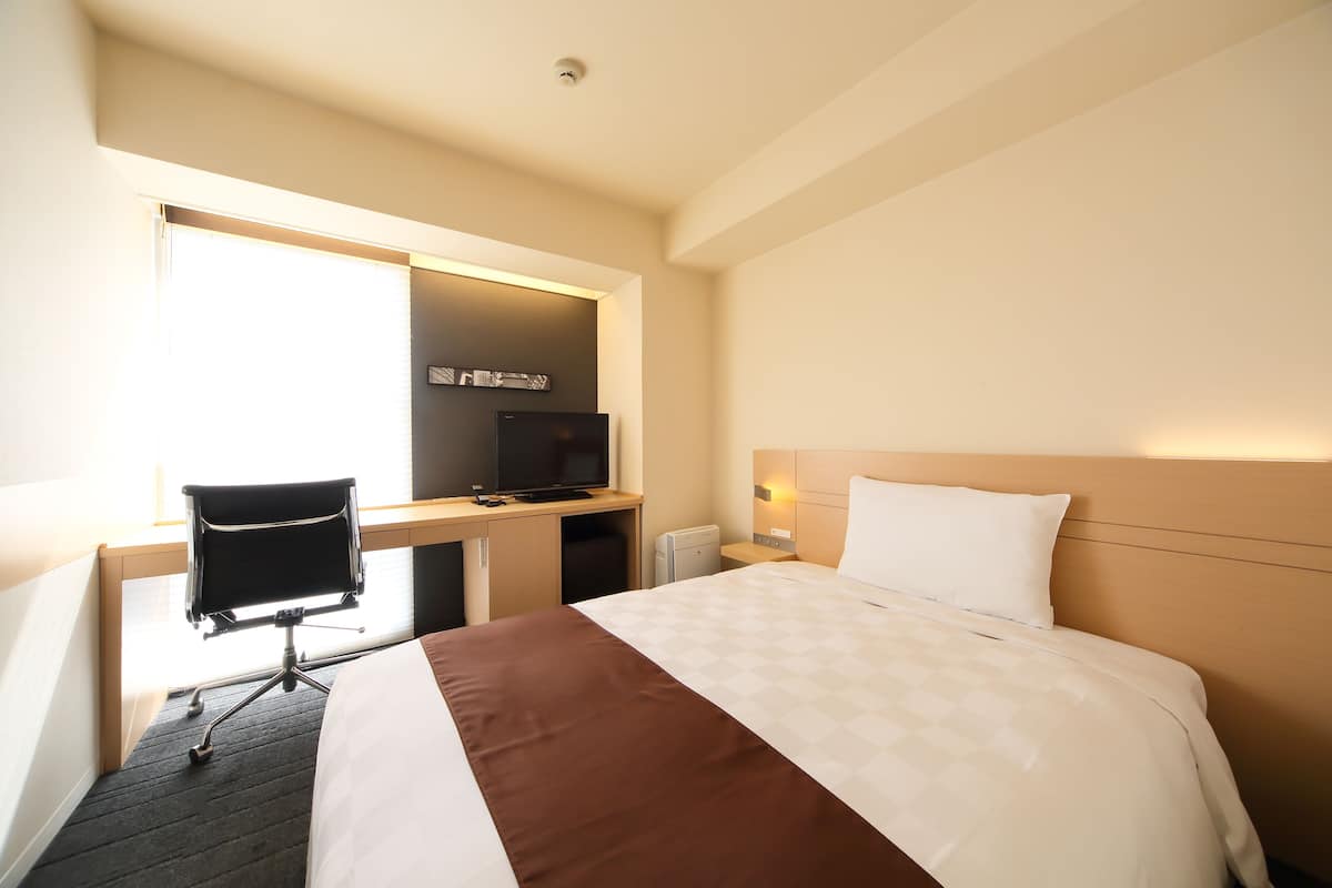 Une chambre d’hôtel avec un lit, un bureau et une chaise, une télévision et une fenêtre.