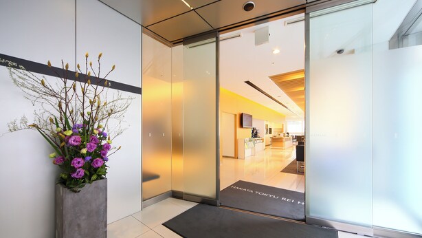 A reception area with a modern interior, a large potted plant, and a glass door leading to the lobby.