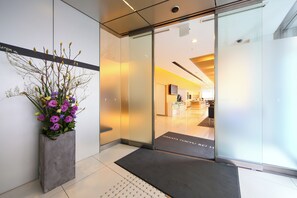 A reception area with a modern interior, a large potted plant, and a glass door leading to the lobby.
