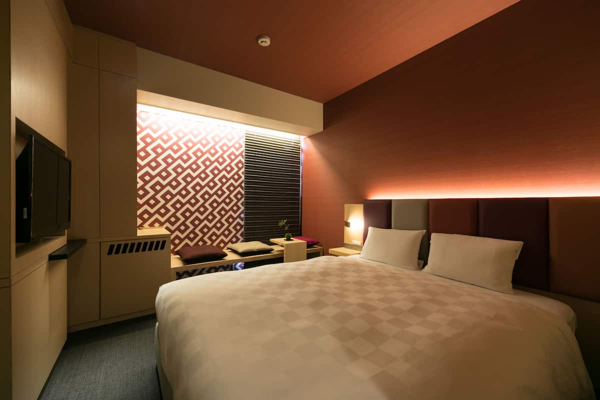 Une chambre d’hôtel avec un grand lit, une télévision, un bureau et une fenêtre décorée.