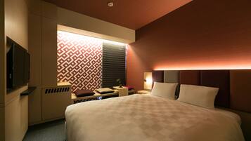 Een hotelkamer met een groot bed, een televisie, een bureau en een raam met een patroon.
