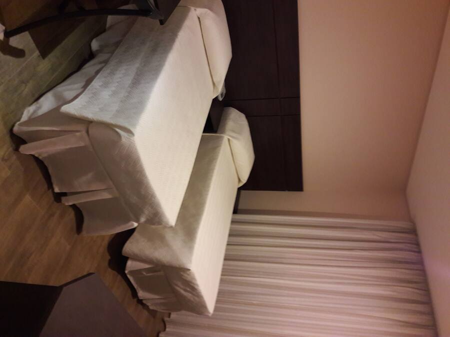 A room with a bed covered in white sheets, a wooden floor, and a dark headboard.