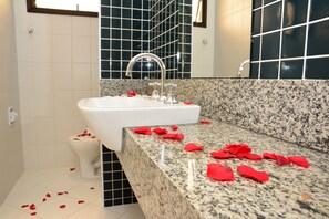 Un baño con lavamanos blanco, paredes de azulejos negros y encimera de granito.